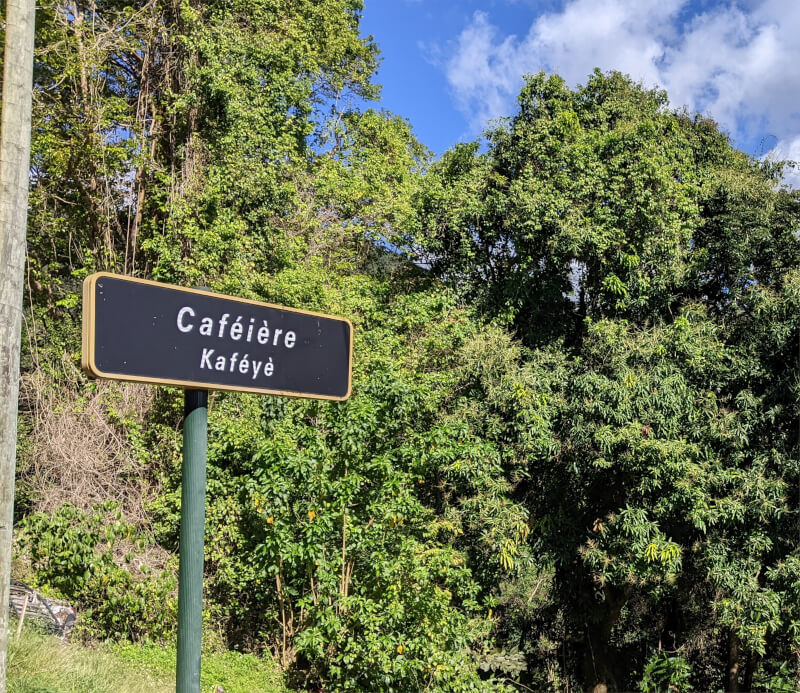 Panneau typique guadeloupéen avec l'incription en français et en Créole, ici devant une plantation de café guadeloupéen.